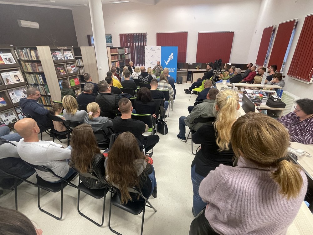 Sala biblioteki wypełniona publicznością podczas spotkania autorskiego